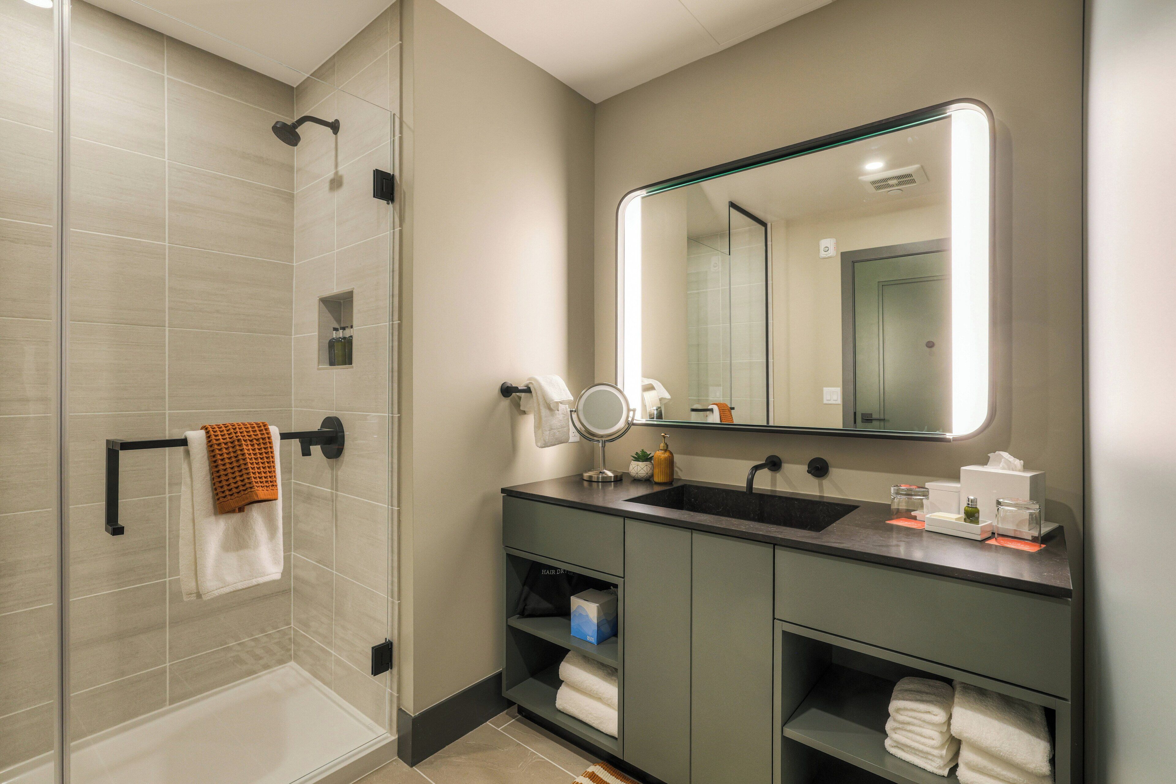 Une salle de bain moderne dotée d’une douche à parois de verre, d’un meuble-lavabo avec un évier, un miroir et un espace de rangement pour les serviettes.