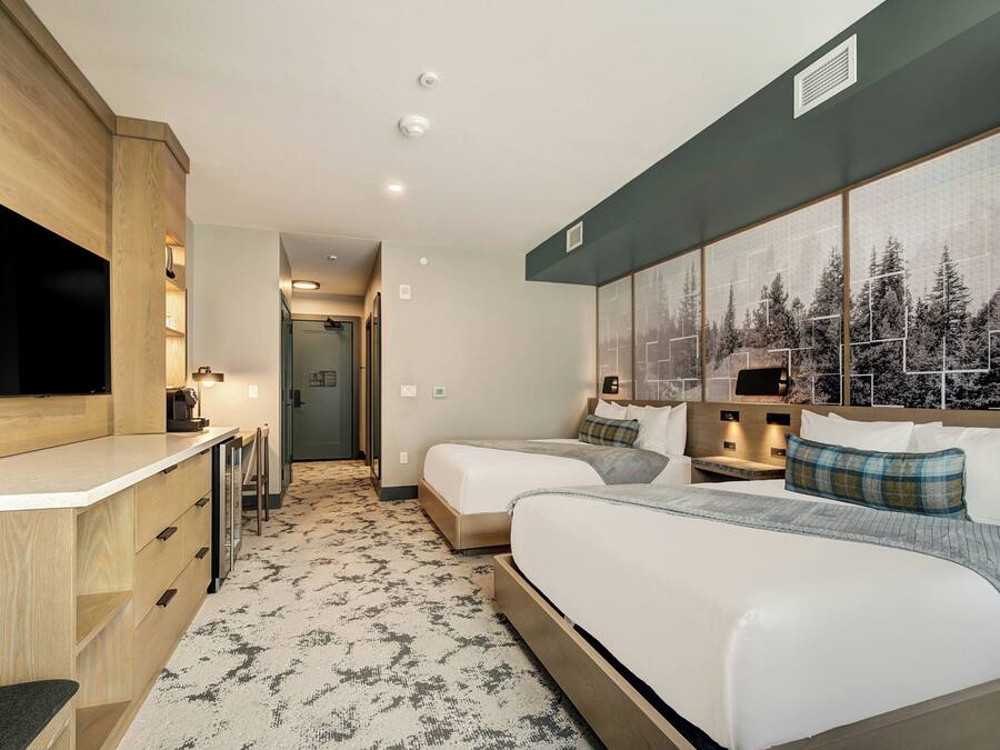 Une chambre d’hôtel avec un lit, un bureau, un miroir et une grande fenêtre donnant sur la forêt.