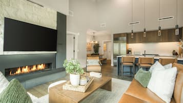 Una sala de estar moderna con chimenea, televisor de pantalla plana, una mesa de centro con objetos decorativos y un sofá con cojines.