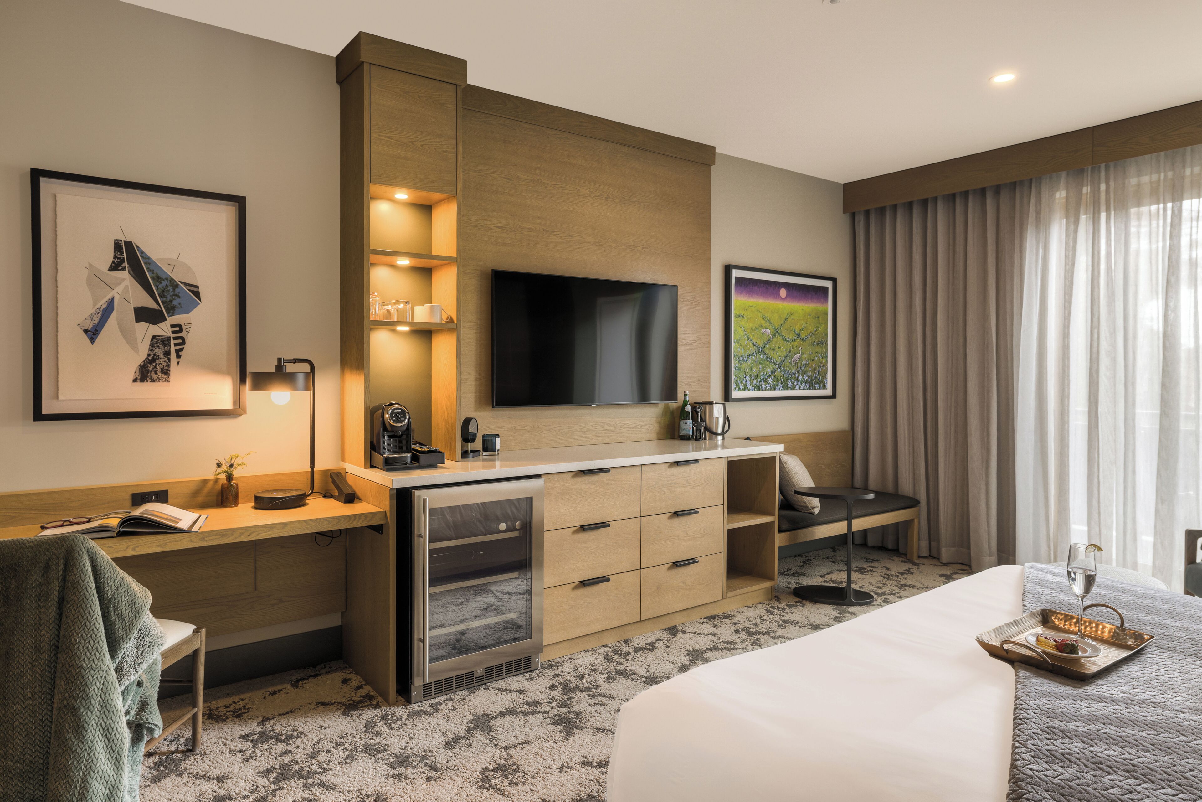 Une chambre d’hôtel comprenant un lit, un bureau avec un téléviseur à écran plat, un minibar, un coin salon et des œuvres d’art aux murs.