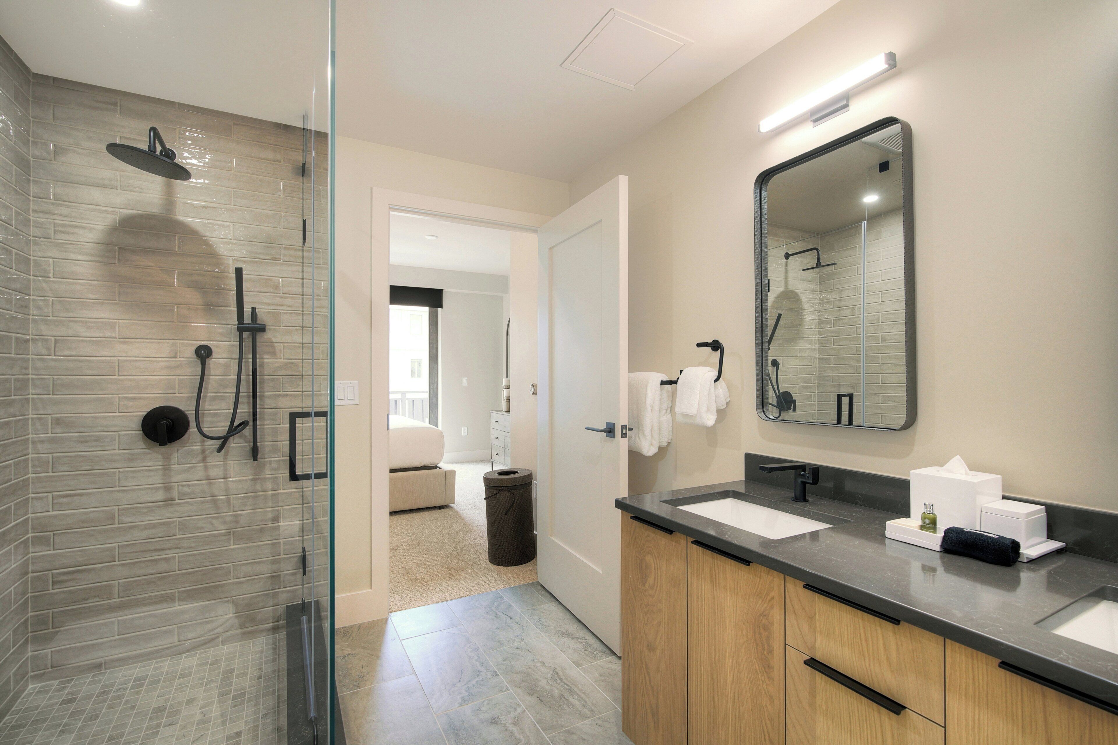 A modern bathroom with a glass-enclosed shower, a large mirror, and a vanity with two sinks.