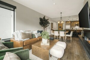A modern living room with a sofa, green armchairs, a coffee table, and a dining area with chairs and a table.