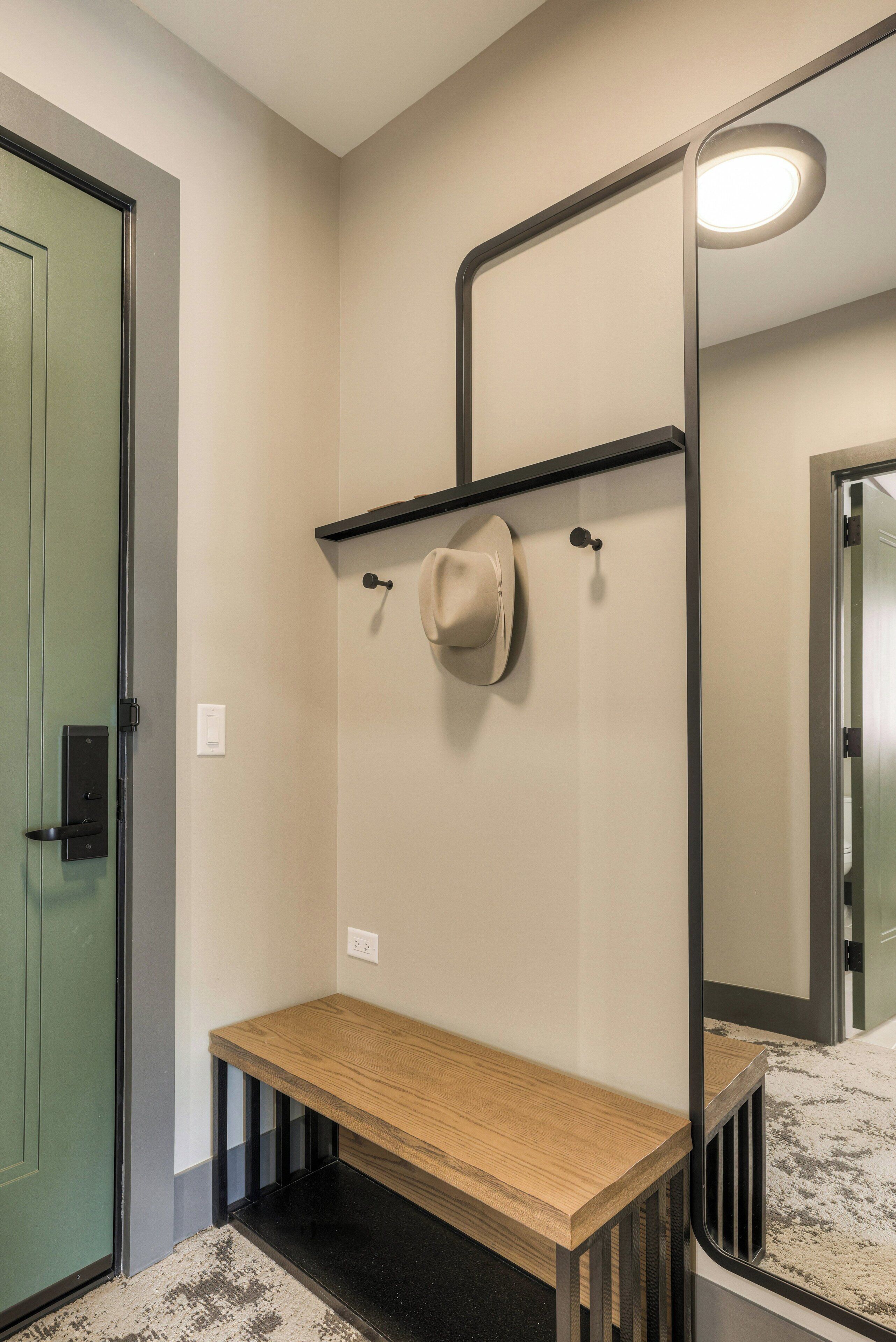 A room with a wooden bench, a mirror, a hat on a hook, and a green door.