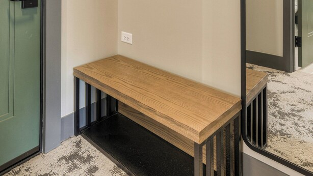 Una habitación con un banco de madera, un espejo, un sombrero colgado en un perchero y una puerta verde.