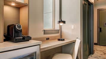 A compact hotel room with a kitchenette, a seating area, a window, and a door.