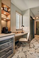 Une chambre d’hôtel de taille réduite, dotée d’une kitchenette, d’un coin salon, d’une fenêtre et d’une porte.