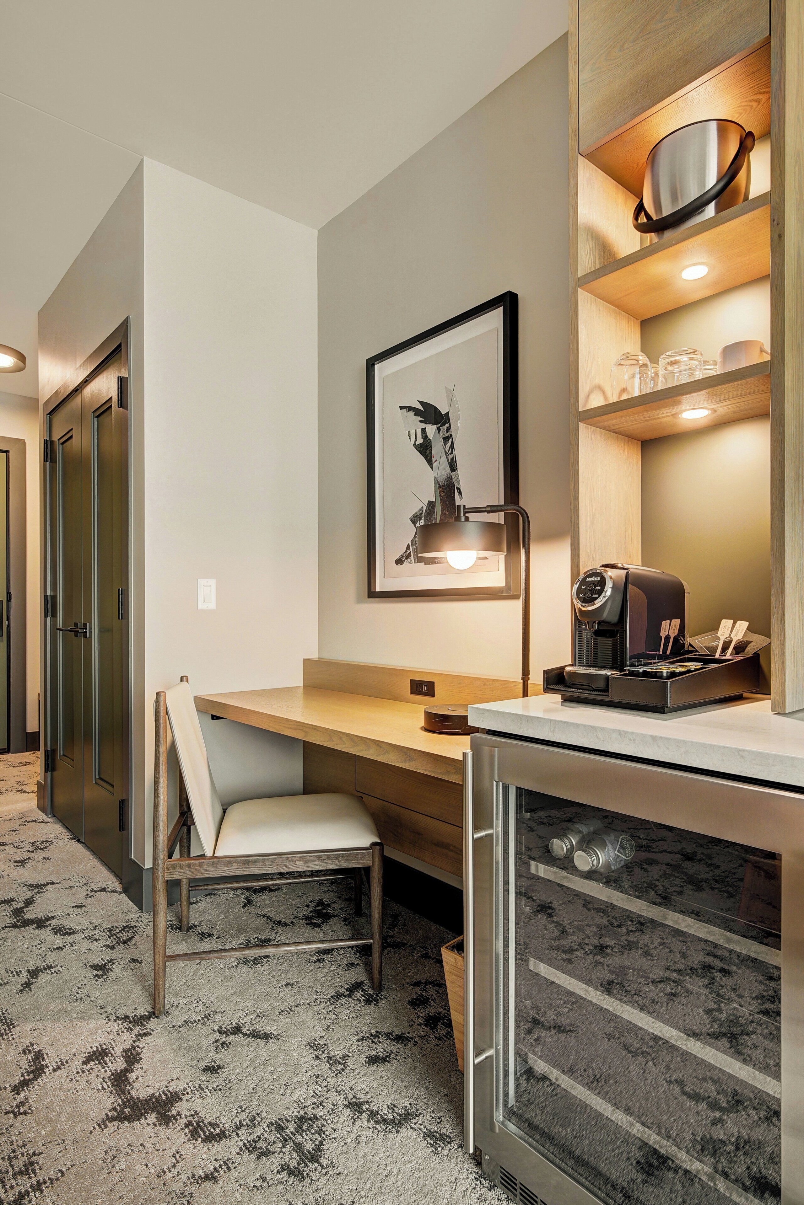 A hotel room with a desk, chair, bed, and a coffee machine.