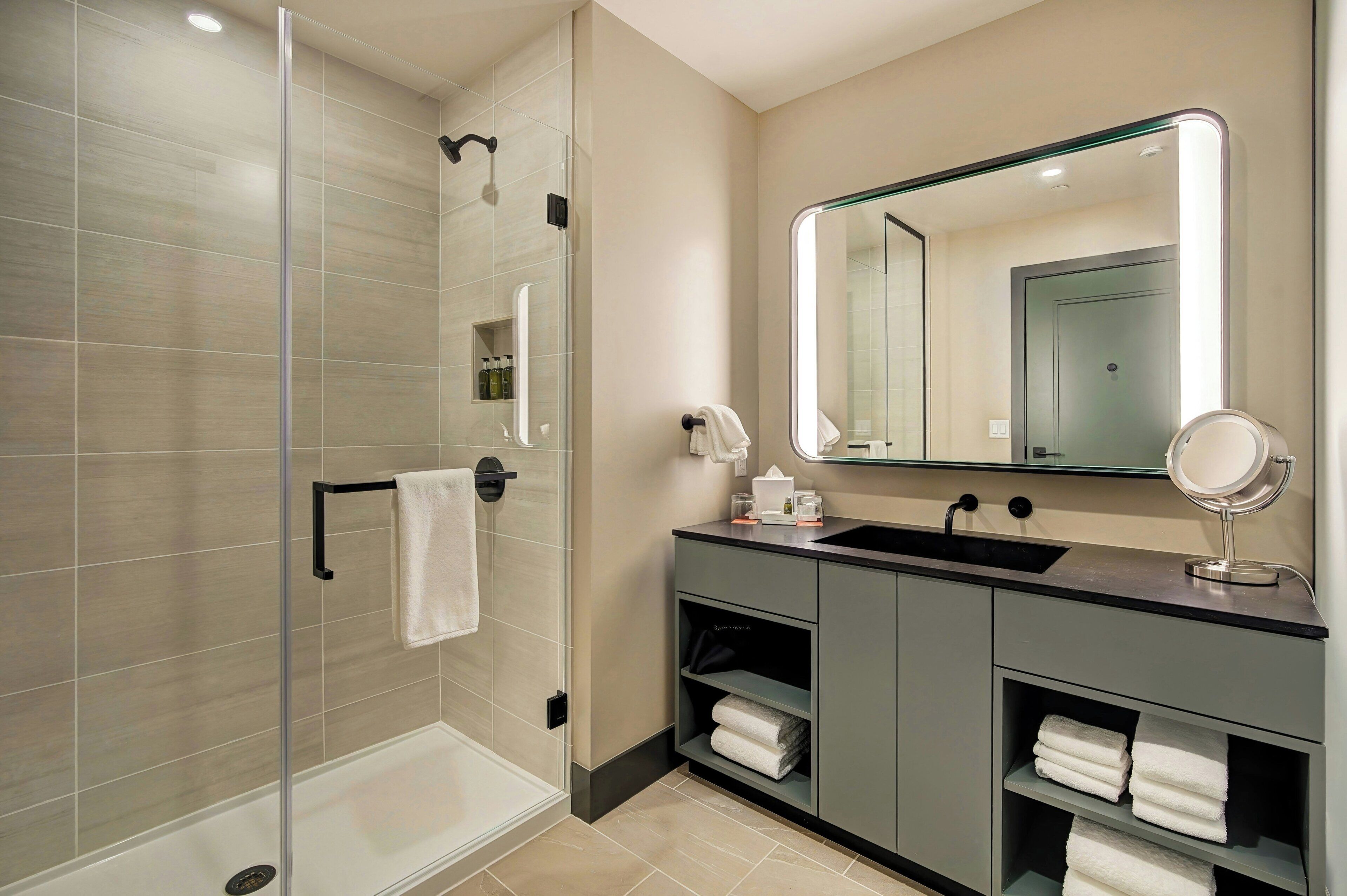 Un baño moderno con ducha de vidrio, tocador con espejo y toallas ordenadas.