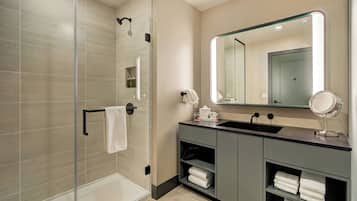 Un baño moderno con ducha de vidrio, tocador con espejo y toallas ordenadas.