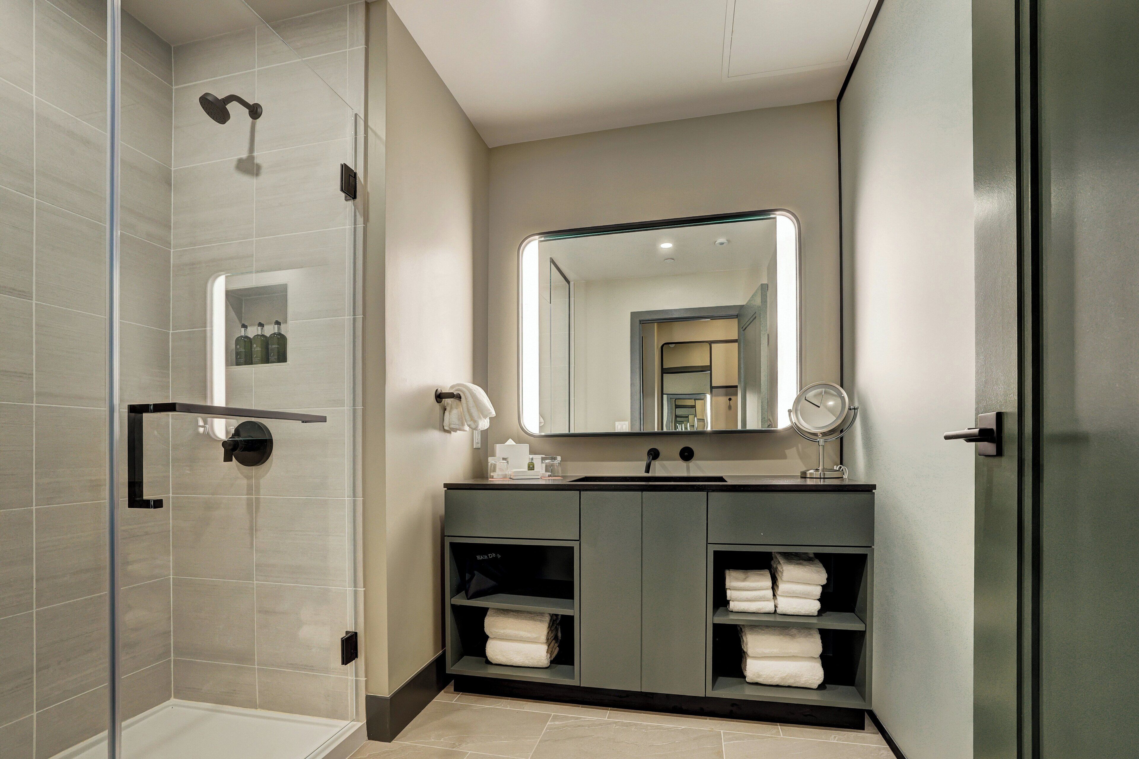 Un baño moderno con ducha, tocador con espejo y un perchero para toallas.