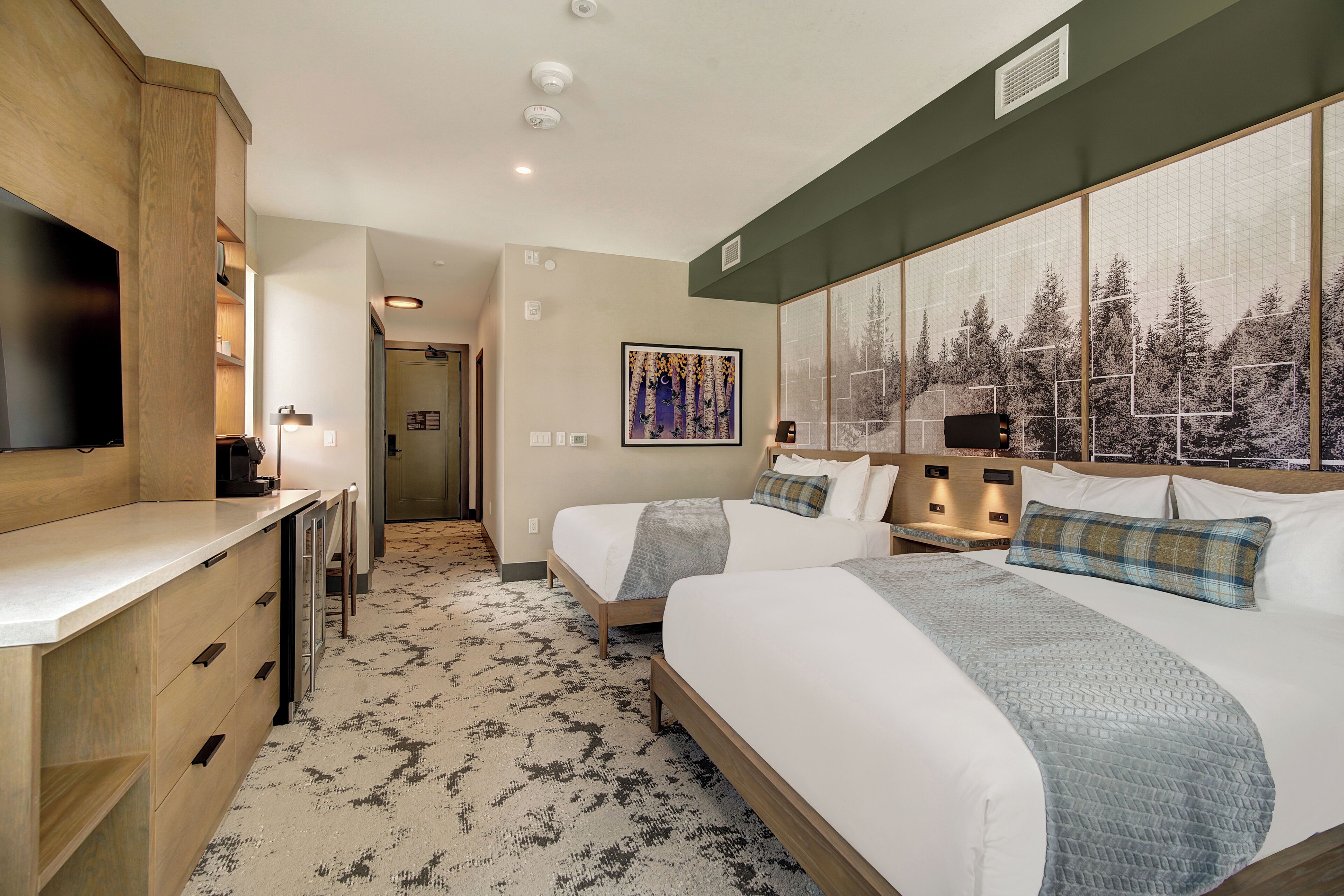 Een hotelkamer met twee bedden, een televisie, een bureau en een groot raam met uitzicht op een bos.