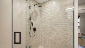 A glass-enclosed shower with a tiled wall, a visible shower control panel, and a door leading to another room.