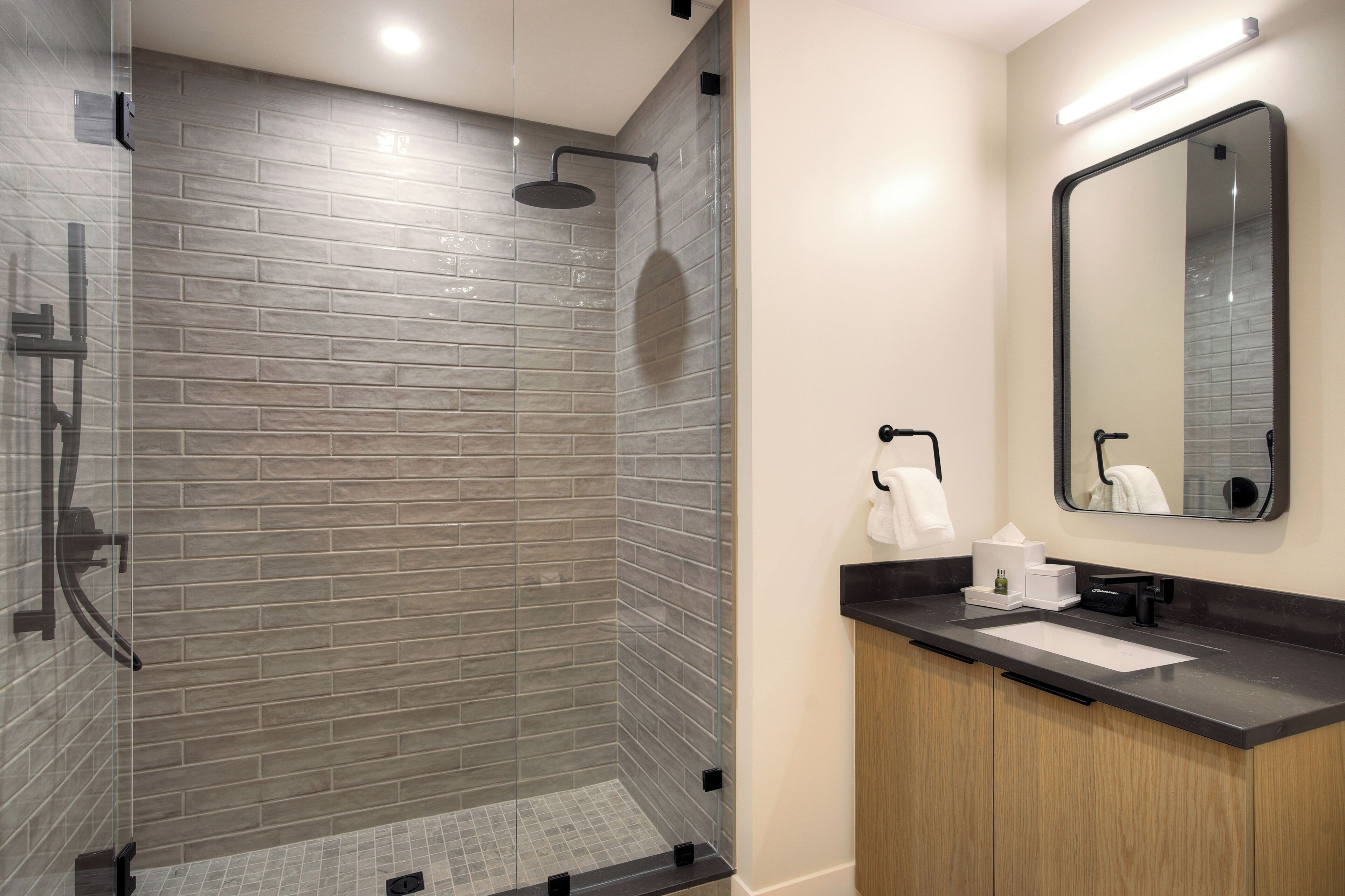 A modern bathroom with a glass-enclosed shower, a wooden vanity, and a large mirror.