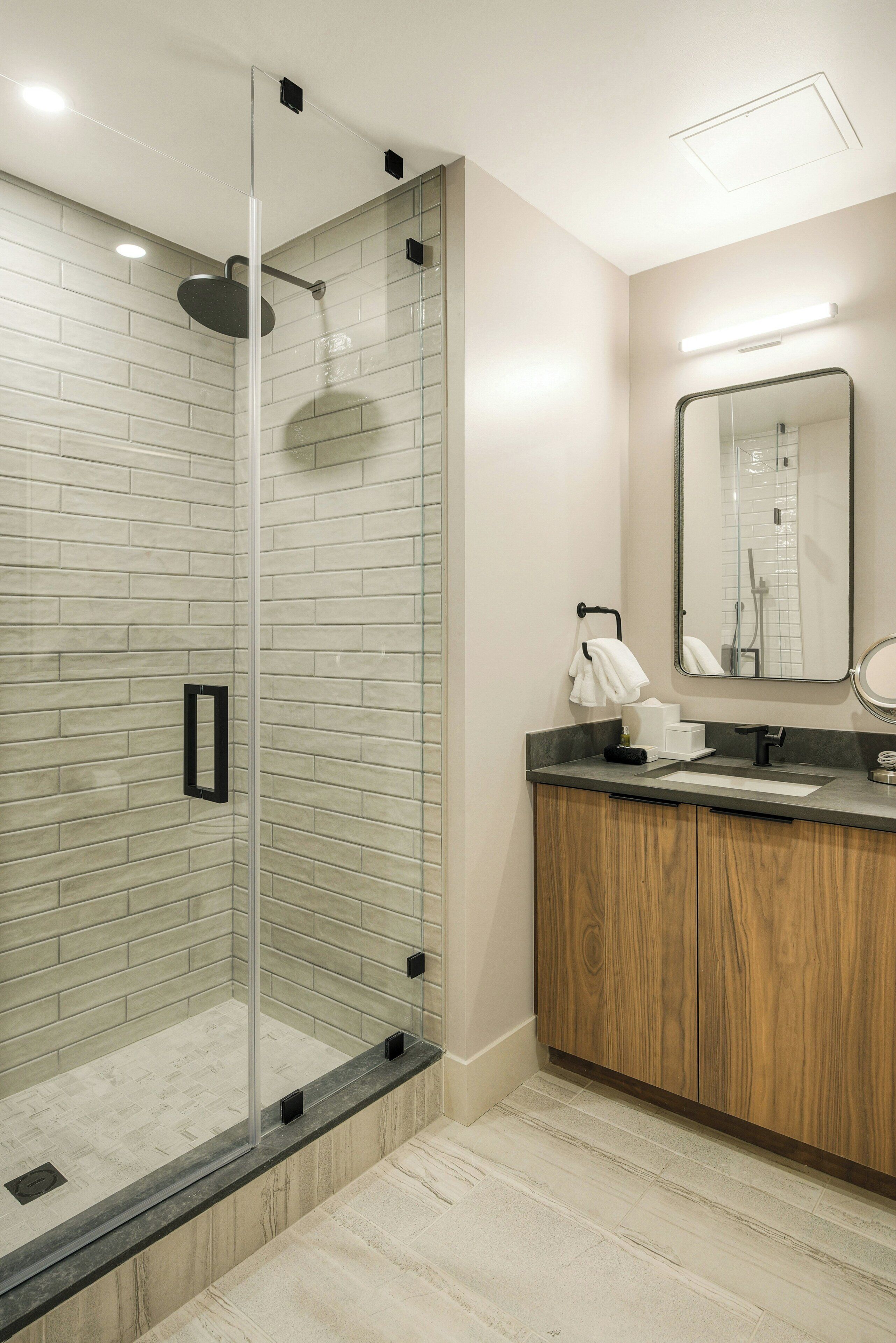 Un baño moderno con cabina de ducha de vidrio, tocador de madera y un espejo grande.