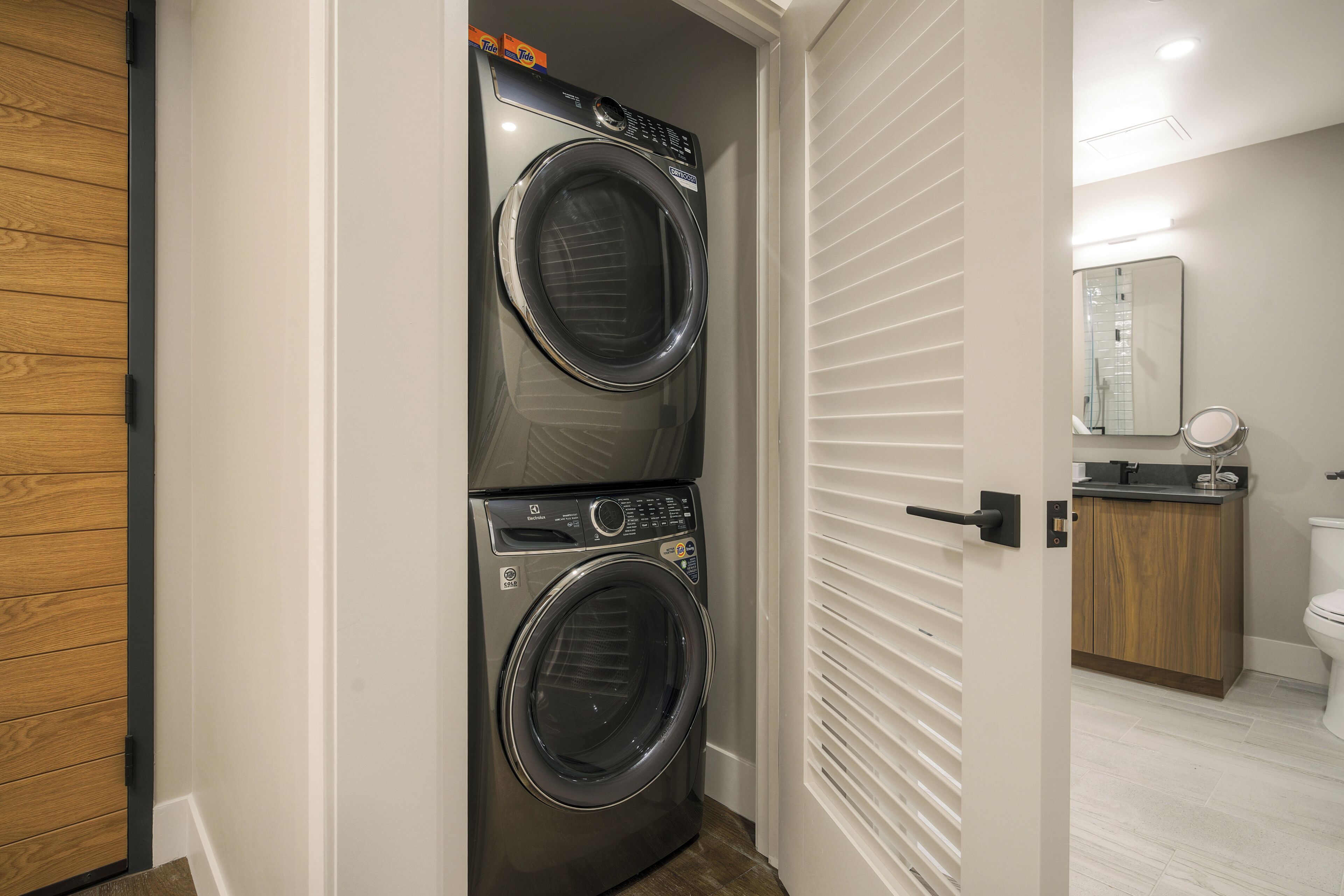 A laundry room with two front-loading washing machines, a wooden door, and a bathroom with a toilet and sink.