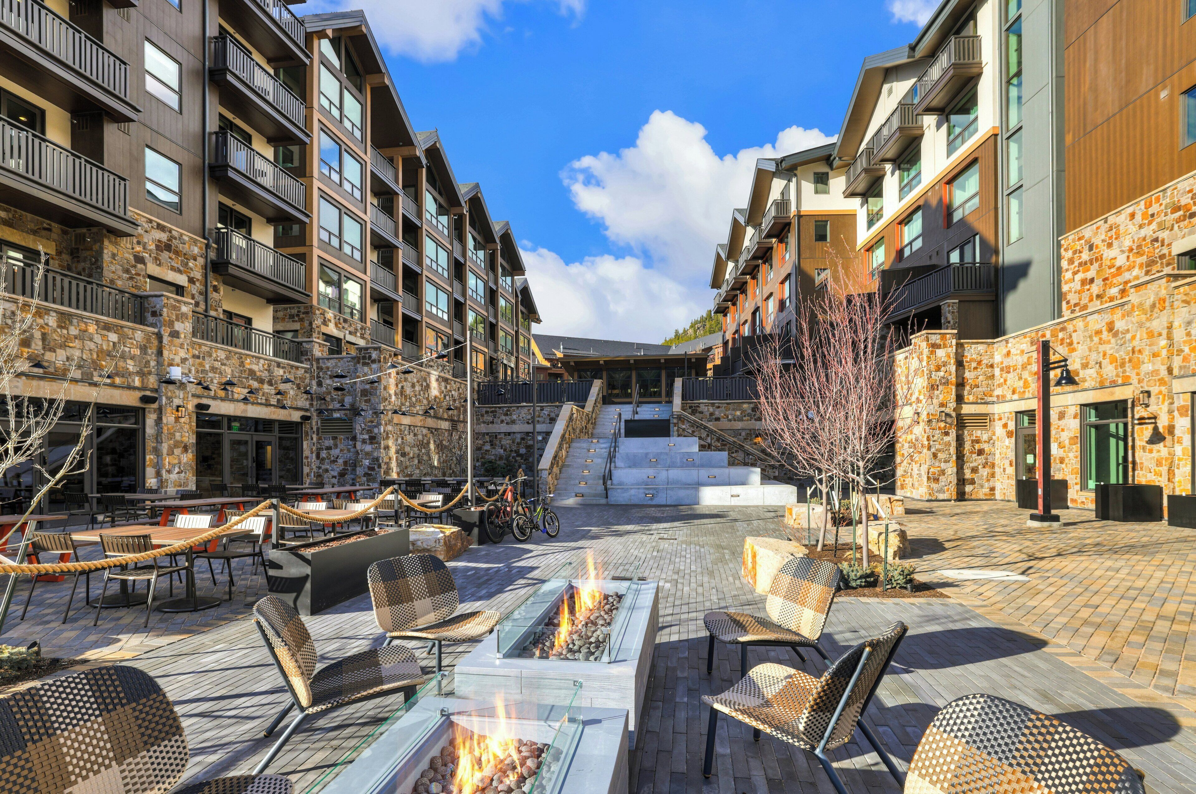 Un patio con mobiliario exterior, una chimenea y una escalera que lleva a los pisos superiores.