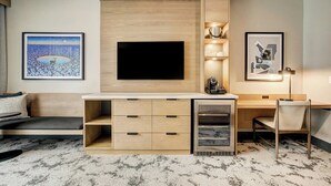 Una habitación de hotel moderna con una televisión de pantalla plana montada en una pared de madera, un escritorio con cajones, una silla y un sofá.