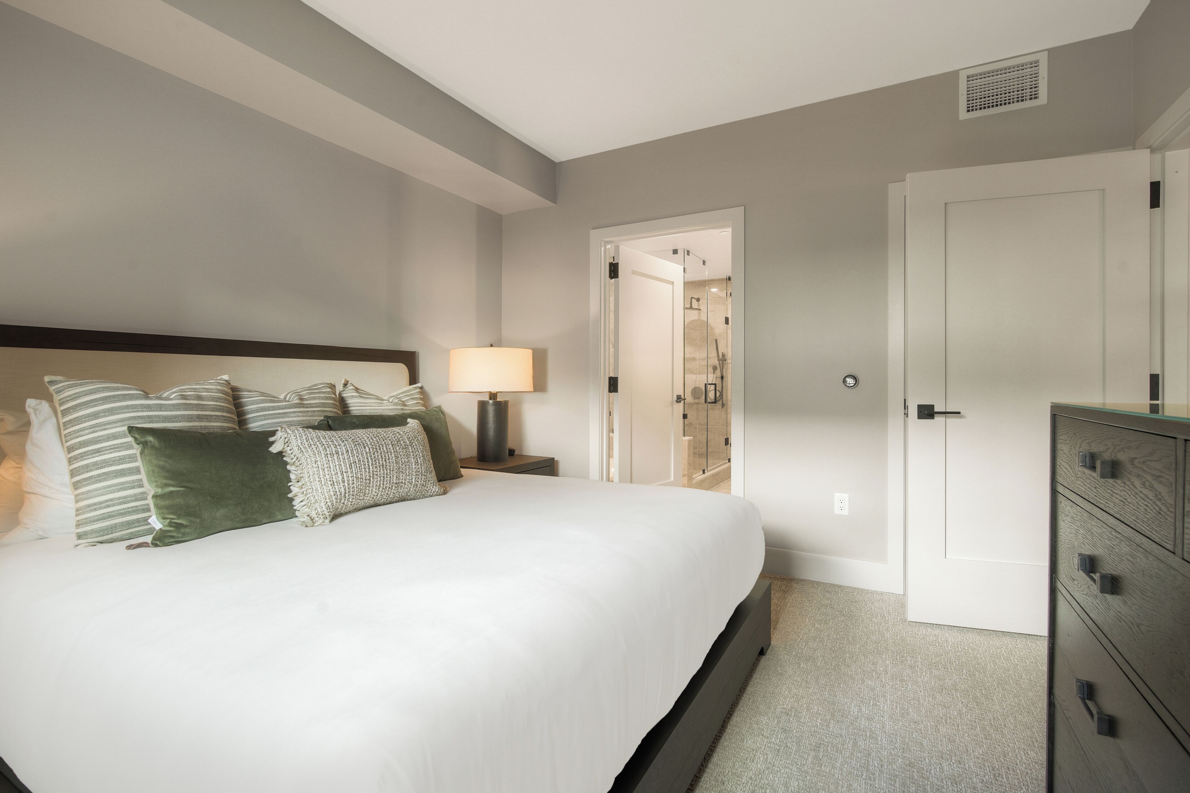 Une chambre d’hôtel avec un grand lit, une table de chevet, une lampe, une armoire et une porte donnant sur une salle de bain.