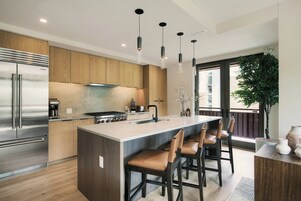 Una cocina moderna con una isla central, electrodomésticos de acero inoxidable e iluminación colgante.