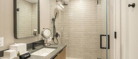 A modern bathroom with a glass shower enclosure, a large mirror, and a vanity with a sink.