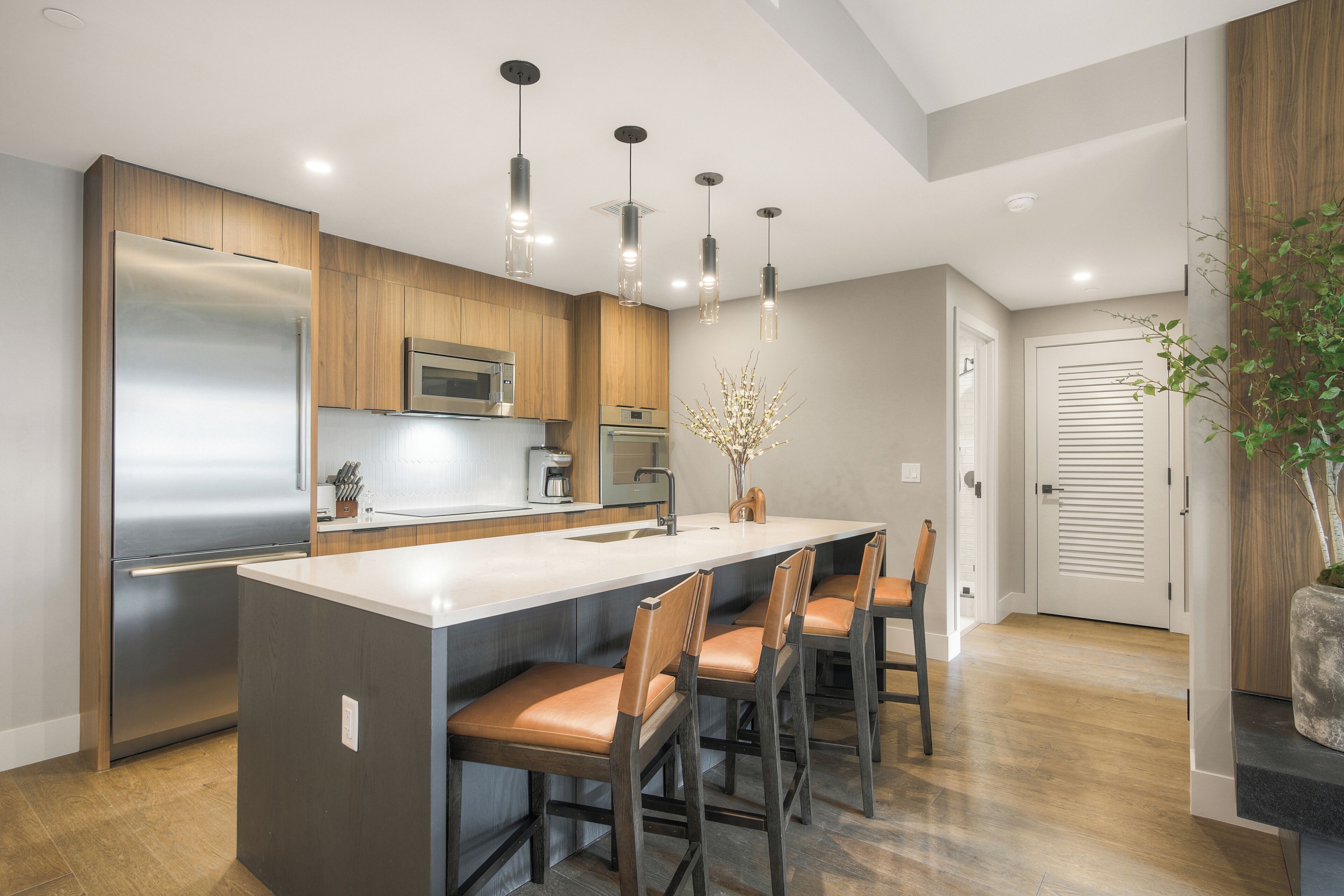 A modern kitchen with a central island, stainless steel appliances, wooden cabinets, and pendant lighting.