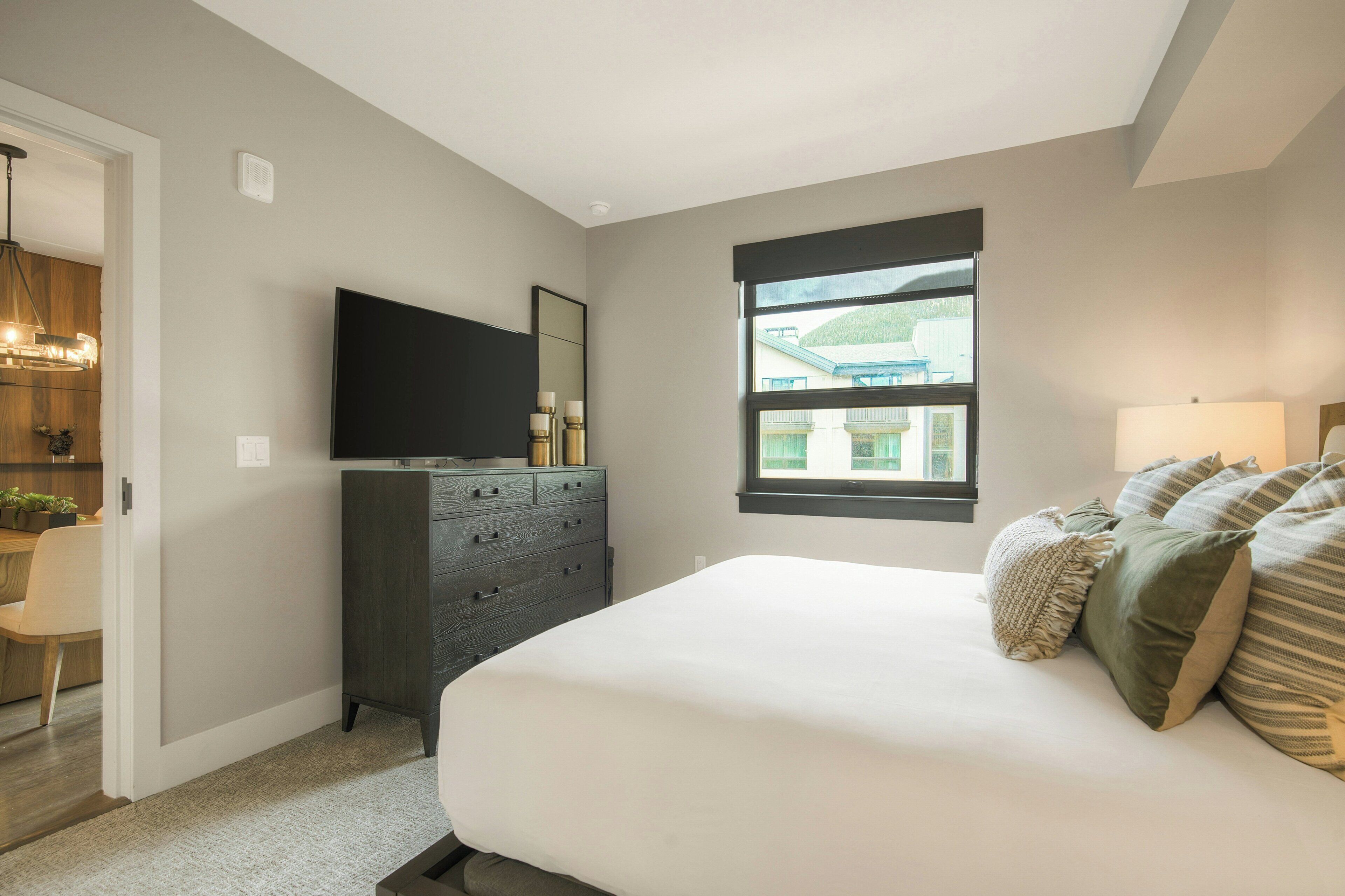 A bedroom with a bed, a dresser, a television, and a window.