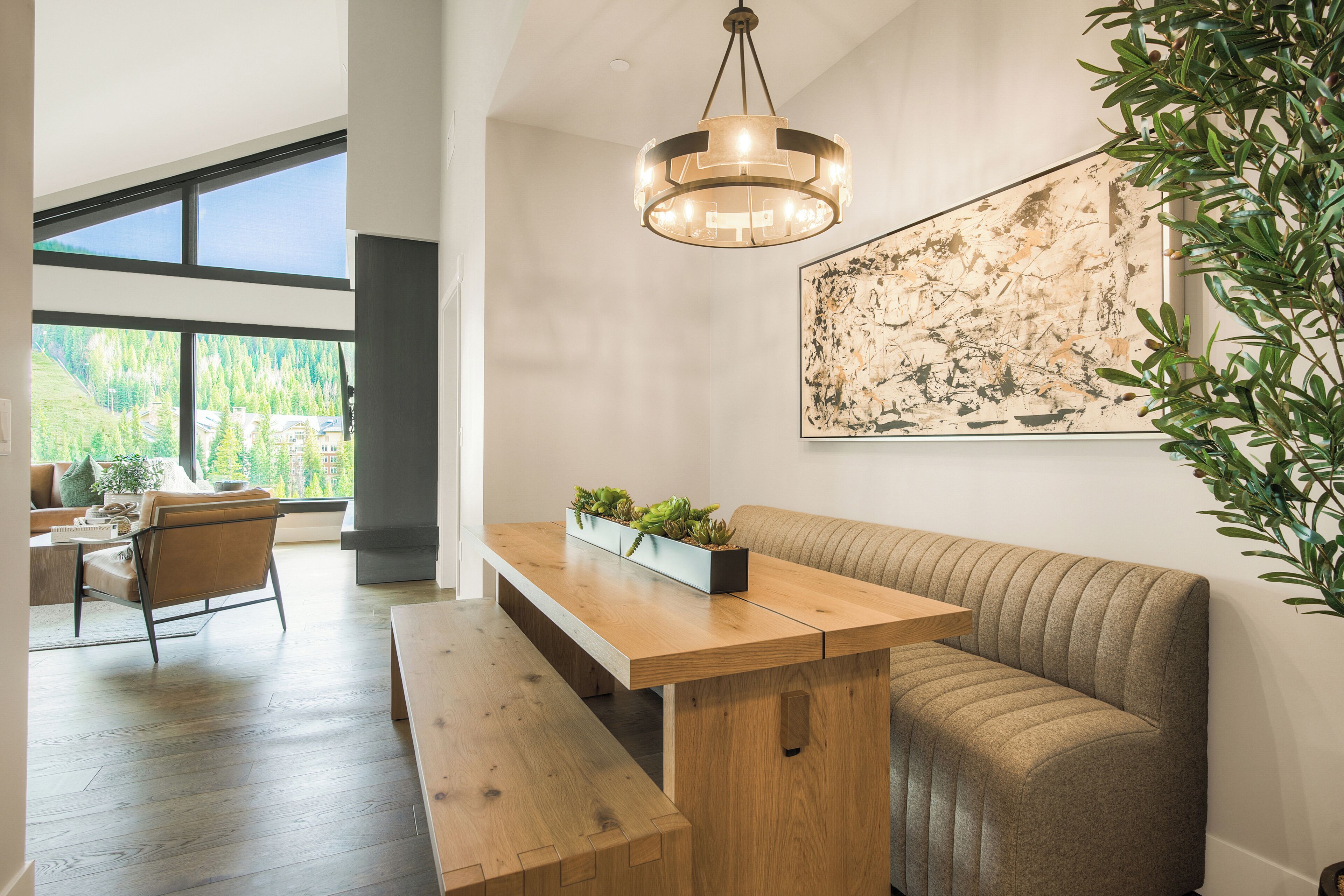A modern interior with a wooden bench, a dining table, a sofa, and a large abstract painting.