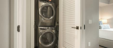 A laundry room with a stacked washer and dryer, a door with a louvered design, and a carpeted floor.