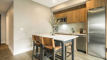 A modern kitchen with a stainless steel refrigerator, wooden cabinets, a marble countertop, and a dining area with a table and chairs.