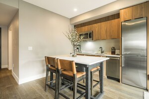 A modern kitchen with a stainless steel refrigerator, wooden cabinets, a marble countertop, and a dining area with a table and chairs.