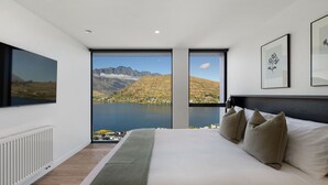 A bedroom with a large bed, a view of mountains and a lake, and two framed pictures on the wall. - The Bunker Charlie C (Queenstown)