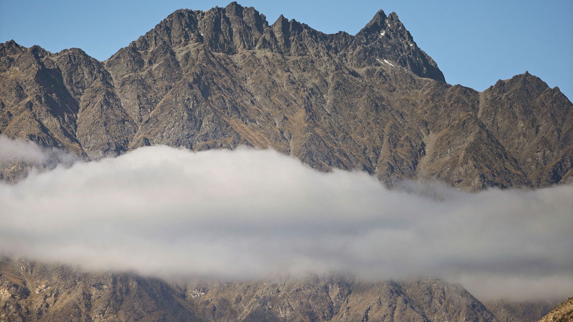 Une chaîne de montagnes aux pics escarpés, avec une couche de nuages à la base.