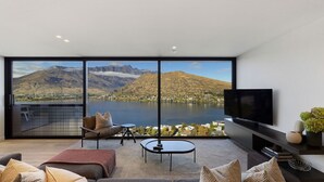 A modern living room with a large window overlooking a lake and mountains, furnished with a sofa, armchair, and coffee table. - The Bunker Charlie C (Queenstown)