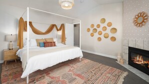 Un lit à baldaquin avec un couvre-lit blanc et des rideaux bruns, un tapis à motifs, une cheminée et des éléments décoratifs sur les murs.
