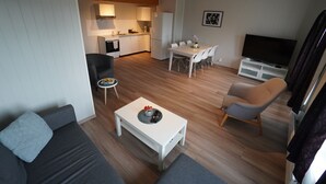 A modern living room with a sofa, a coffee table, a TV stand, and a dining area. - Træna Overnatting (Traena)