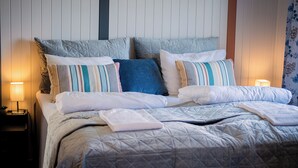 A neatly made bed with a quilted bedspread and multiple pillows, including striped and solid colors. - Træna Overnatting (Traena)