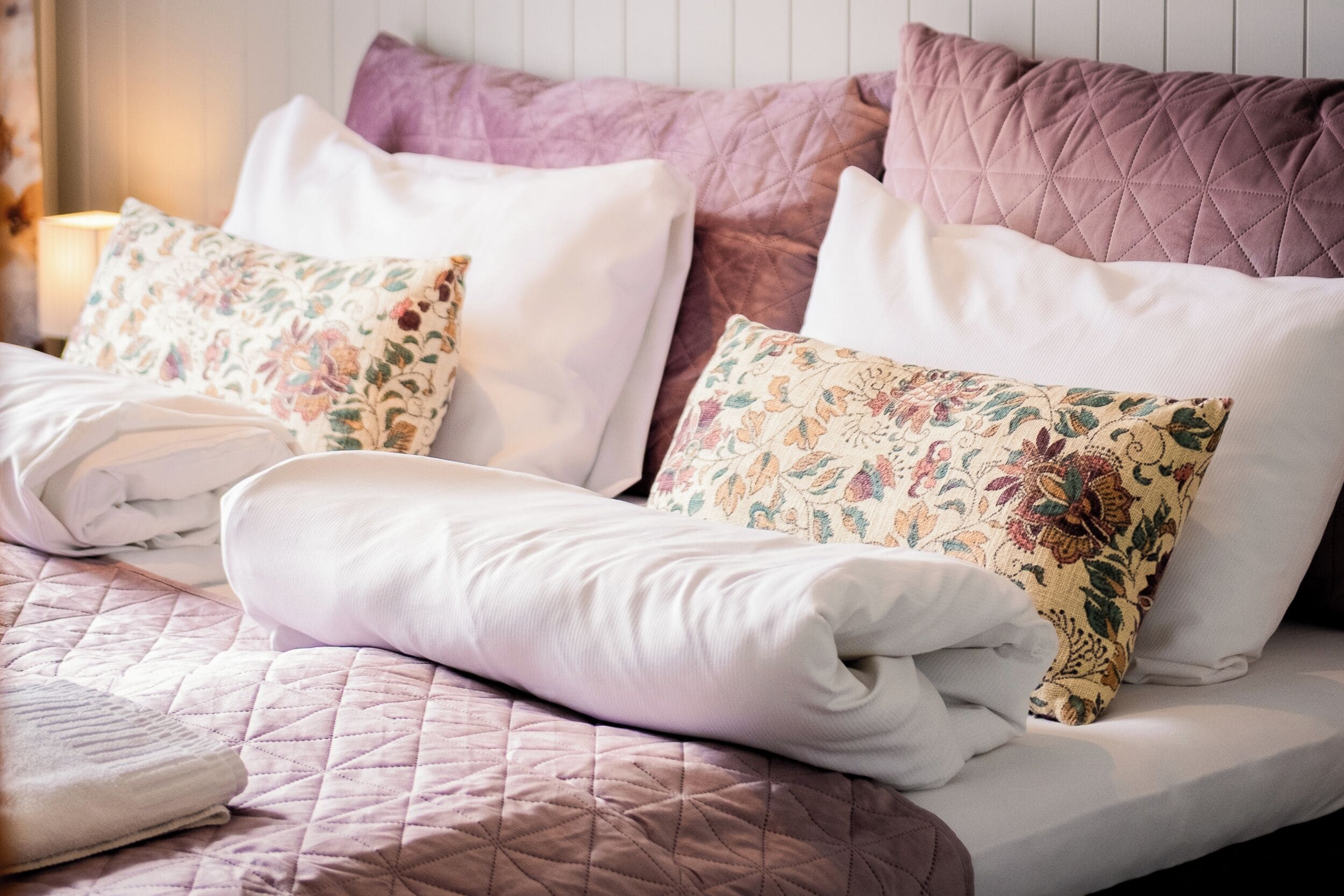 A neatly made bed with a quilted bedspread, two floral-patterned pillows, and a white blanket.