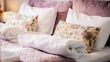 Una cama bien hecha con una colcha acolchada, dos almohadas estampadas con motivos florales y una manta blanca.