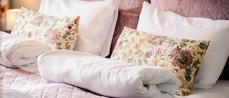 A neatly made bed with a quilted bedspread, two floral-patterned pillows, and a white blanket.