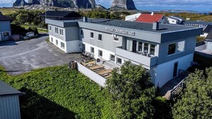 A modern building with a sign reading "TRANA OVERNATING" in a scenic area with mountains in the background. - Træna Overnatting (Traena)