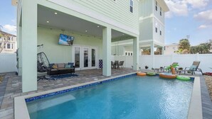 A swimming pool with a covered patio area, outdoor furniture, and inflatable toys.