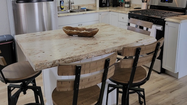Una cocina moderna con armarios blancos, electrodomésticos de acero inoxidable, una isla de madera con taburetes y un ventilador de techo.