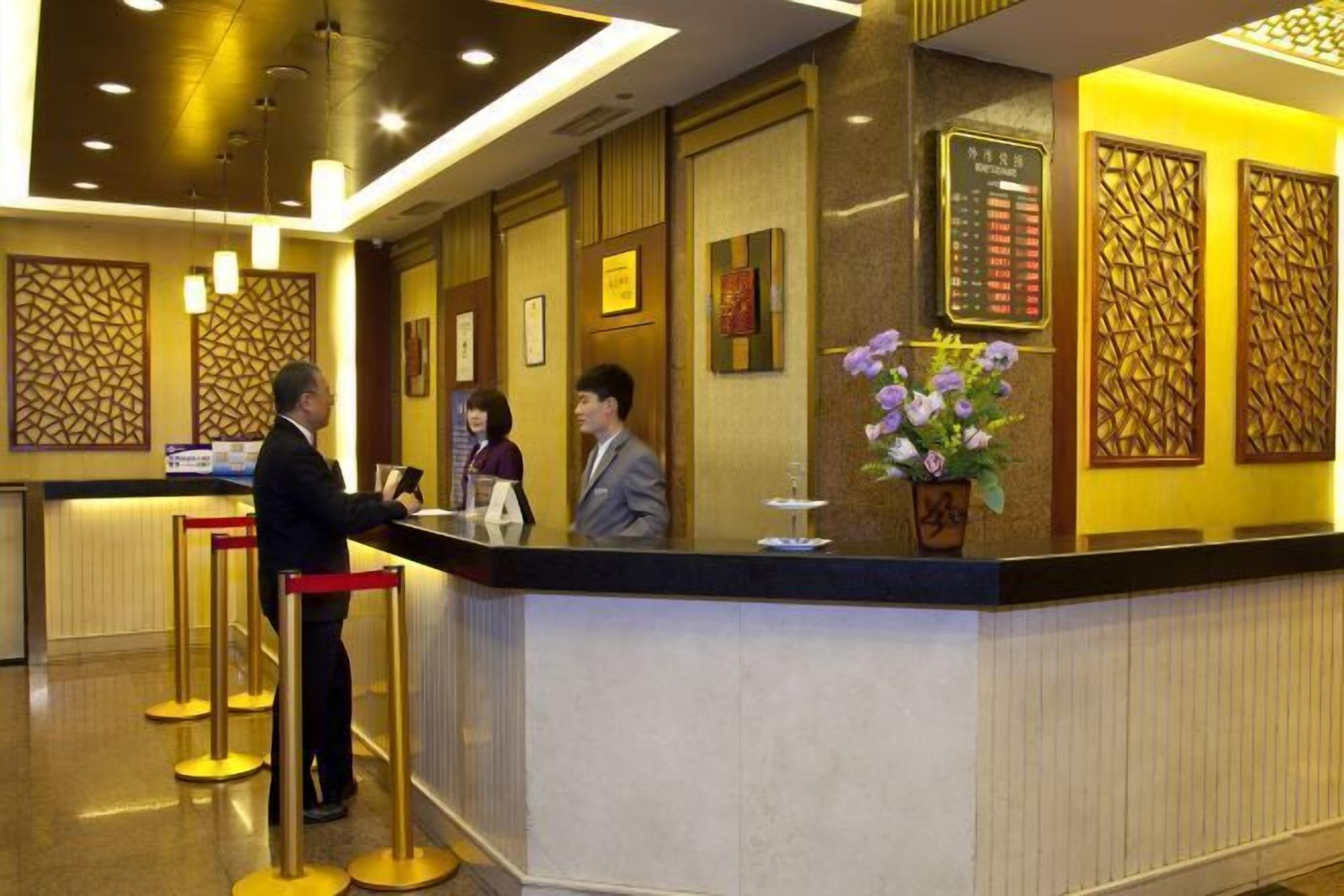 Zona de recepción de un hotel, con mostrador de recepción, atención al cliente y una pared decorativa con patrones geométricos.