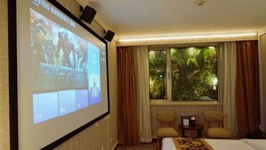 A hotel room with a large screen displaying a movie, a bed, two chairs, a window with a view of greenery, and a carpet with a floral pattern. - Chongwenmen Hotel（Near metro,Tian’anmen Square,Wangfujing,Forbidden city And Temple of heaven） (Beijing)