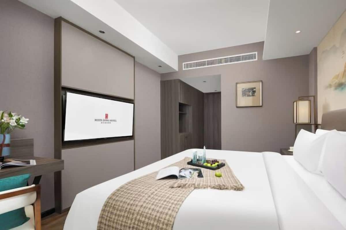 A hotel room with a bed, a TV, a desk, and a window.