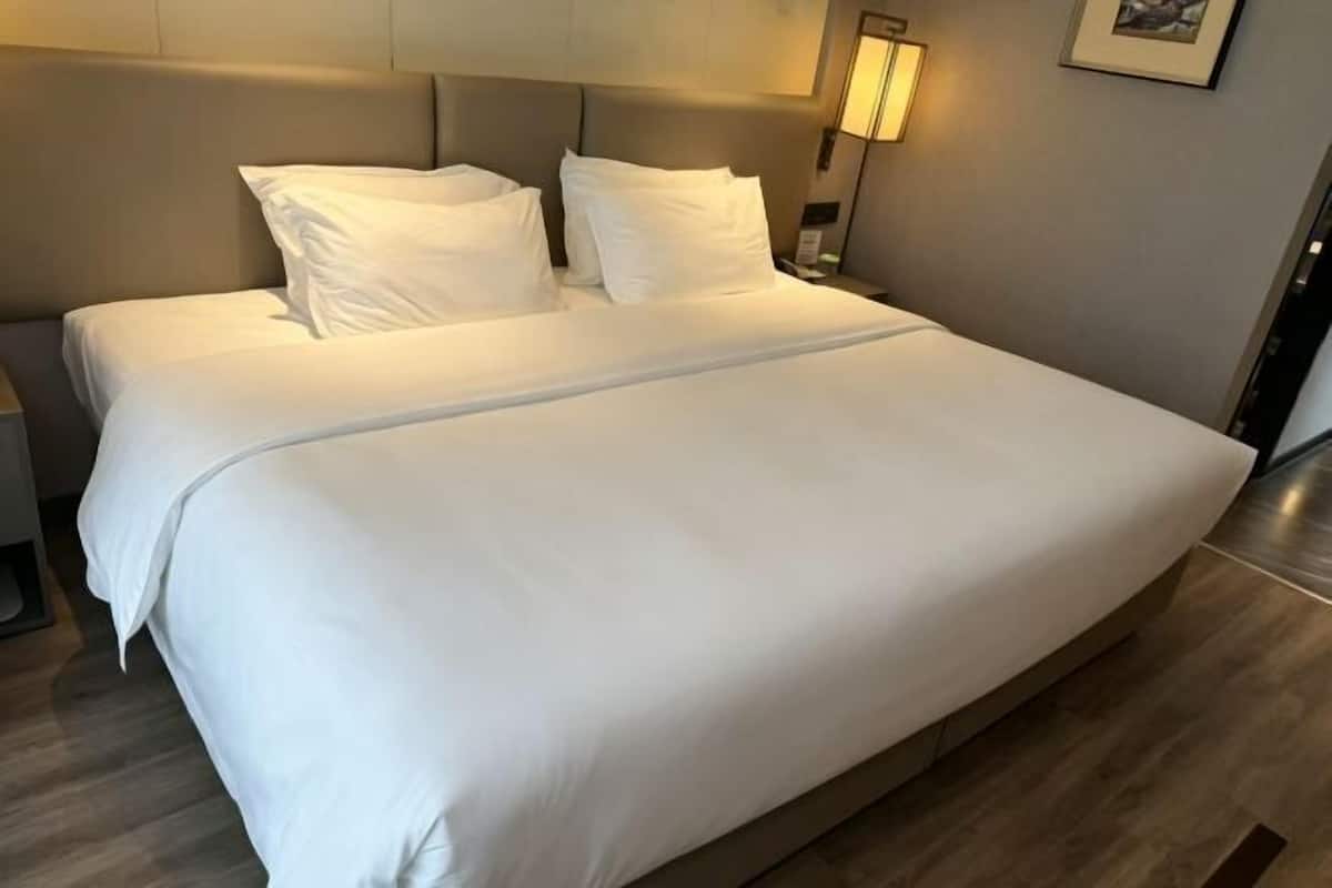 A large bed with white linens, a headboard, and a bedside lamp.