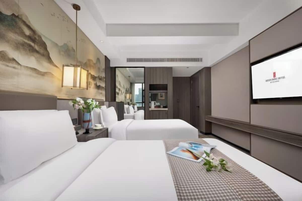 A hotel room with a bed, bedside tables, a TV, and a painting on the wall.