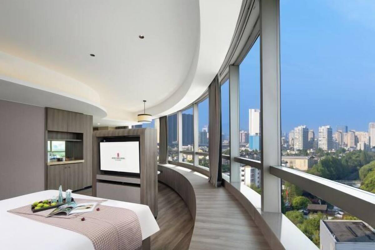 A modern hotel room with a curved balcony, a large TV screen, and a city view.