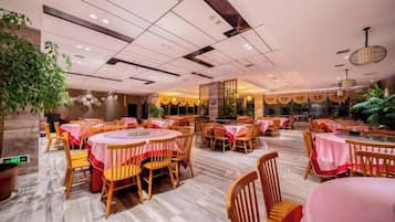 A spacious restaurant with round tables and chairs, a polished floor, and a modern ceiling design.