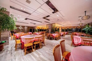 Un restaurante espacioso con mesas y sillas redondas, piso pulido y un diseño moderno en el techo.
